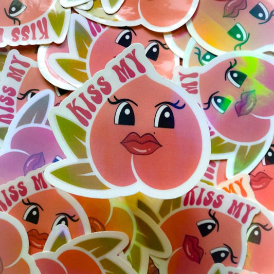 Sticker that Says: “Kiss my” sitting to the side of a female cartoon peach   background: white